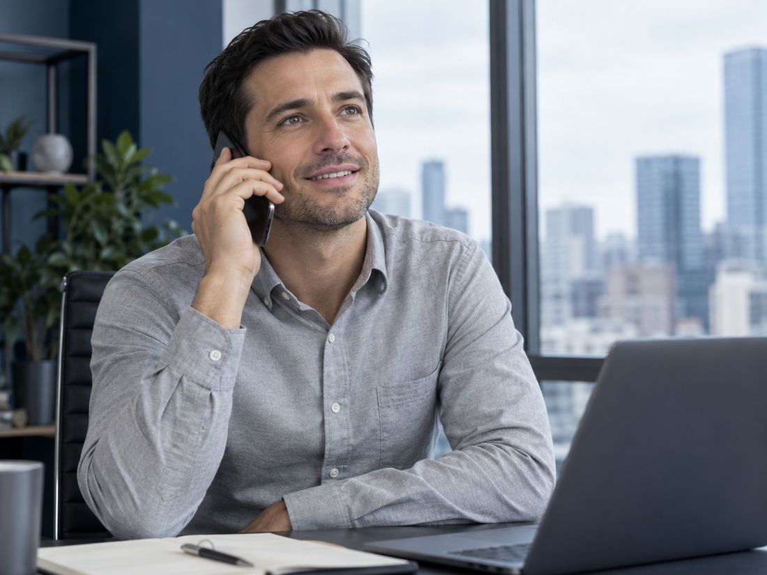 A man at his office desk calls the dental practice on his smartphone